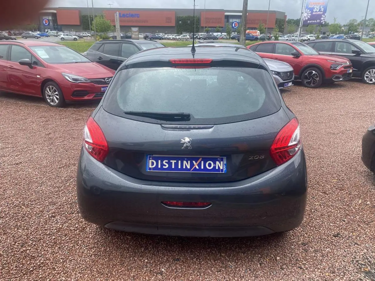 Vue arrière d'une Peugeot 208 gris shark 2013 avec plaque Distinxion sur un parking extérieur.