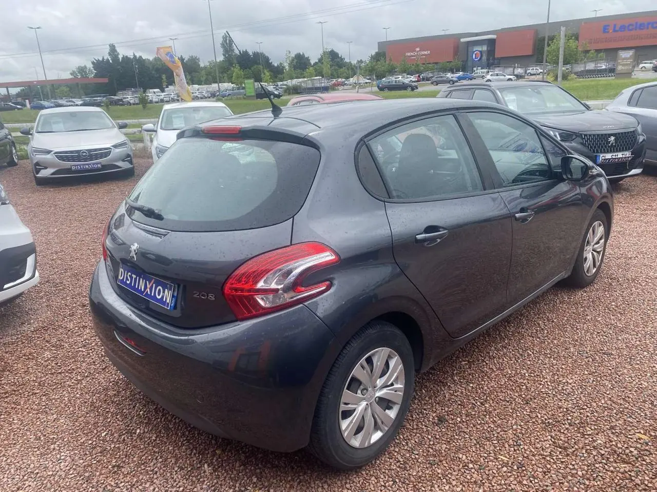 Peugeot 208 gris shark vue 3/4 arrière droit sur parking, avec feux arrière et antenne de toit visibles.