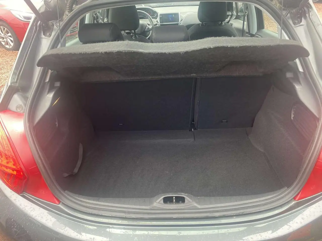Coffre ouvert d'une Peugeot 208 gris shark, vue arrière montrant l'intérieur spacieux et la plage arrière relevée.