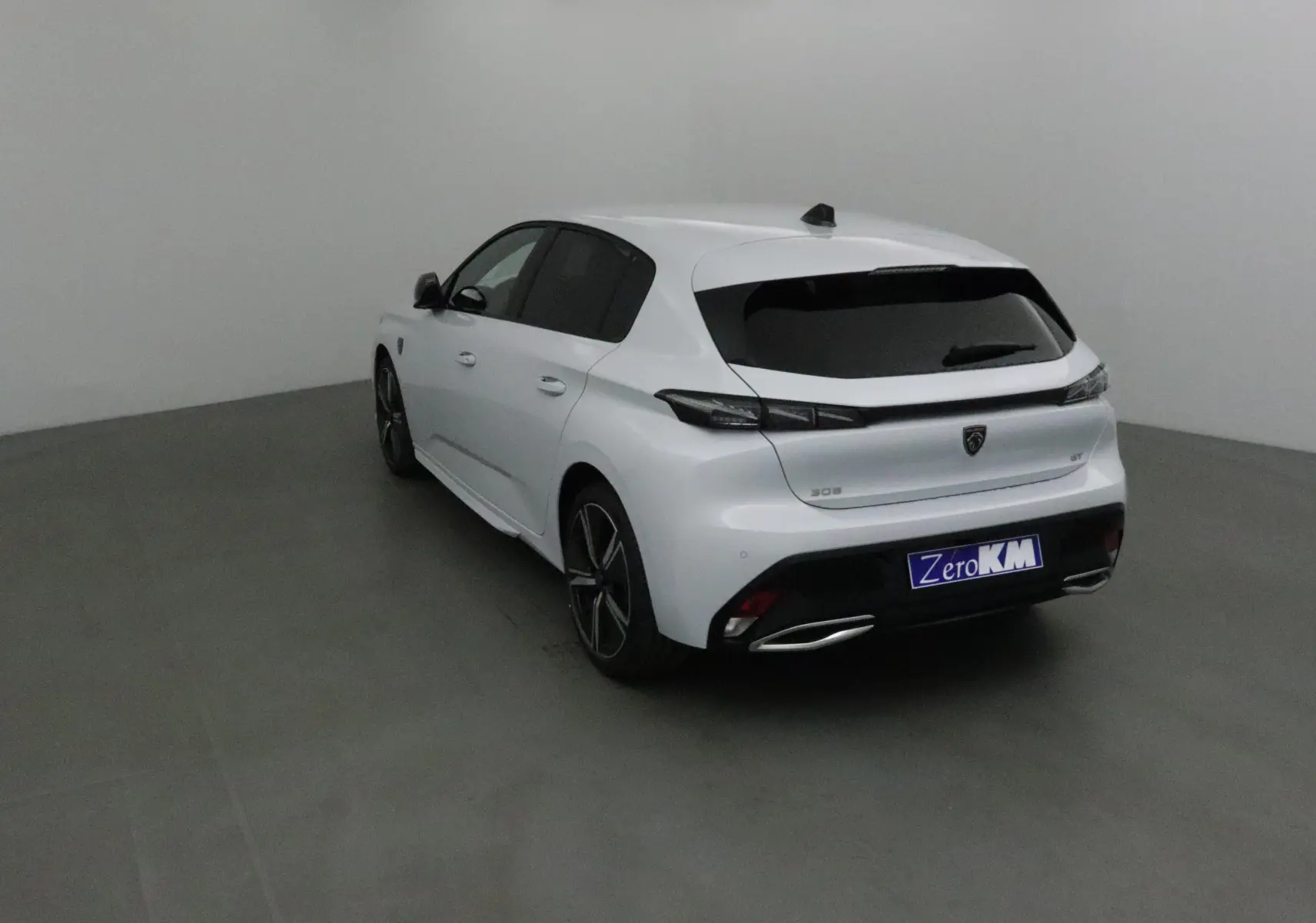 Peugeot 308 blanc Okenite vue 3/4 arrière droit dans un studio, avec vitres teintées et jantes alliage noires.