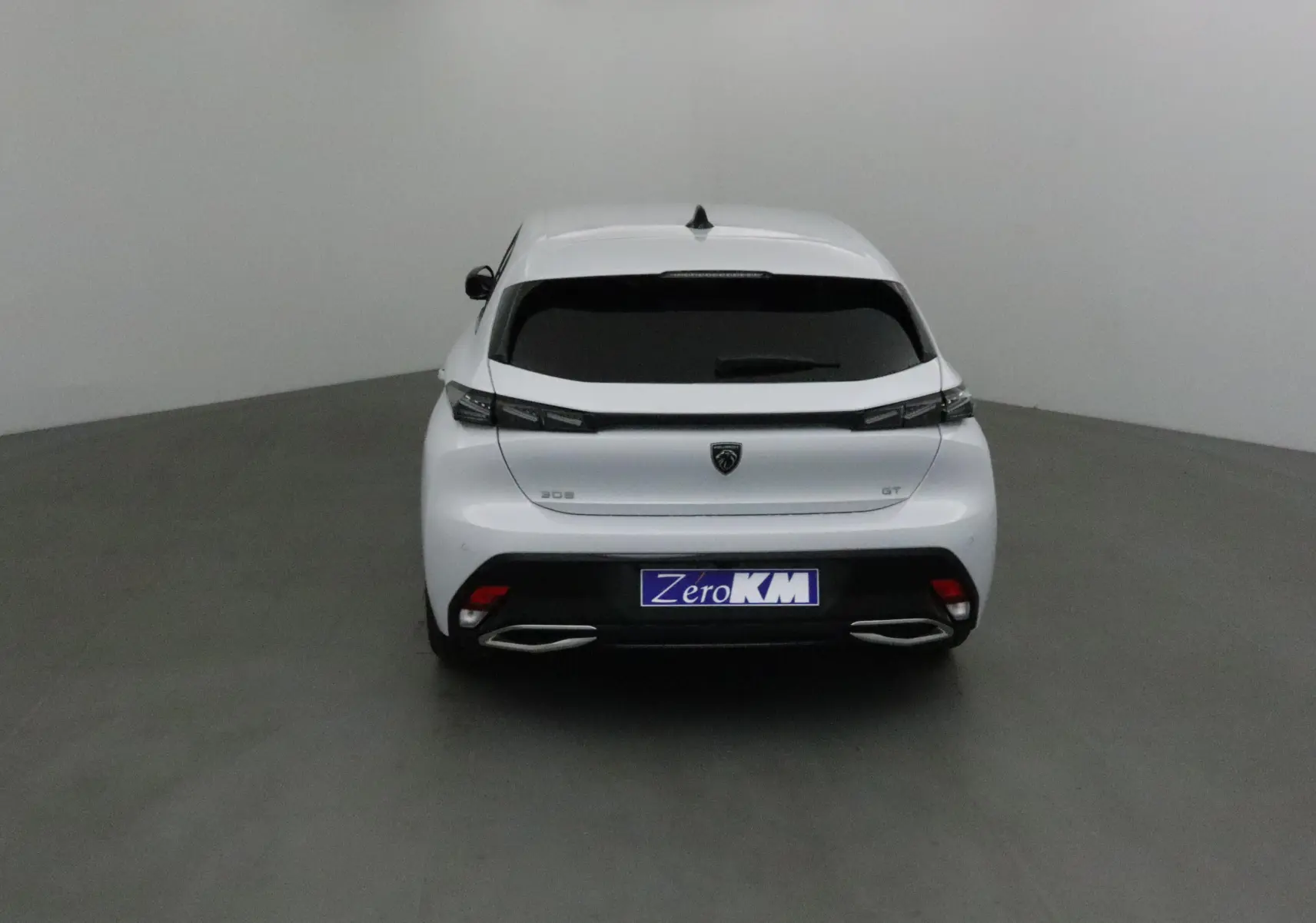 Vue arrière d'une Peugeot 308 GT blanche Okenite 2025 avec feux effilés et double sortie d'échappement chromée.