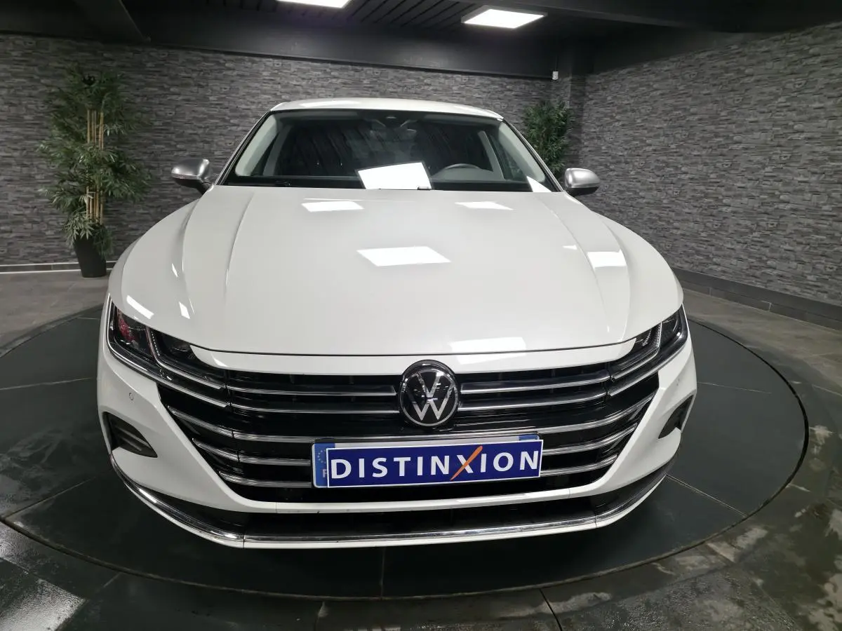 Vue avant d'une Volkswagen Arteon blanche avec calandre horizontale noire et logo VW centré dans un showroom.