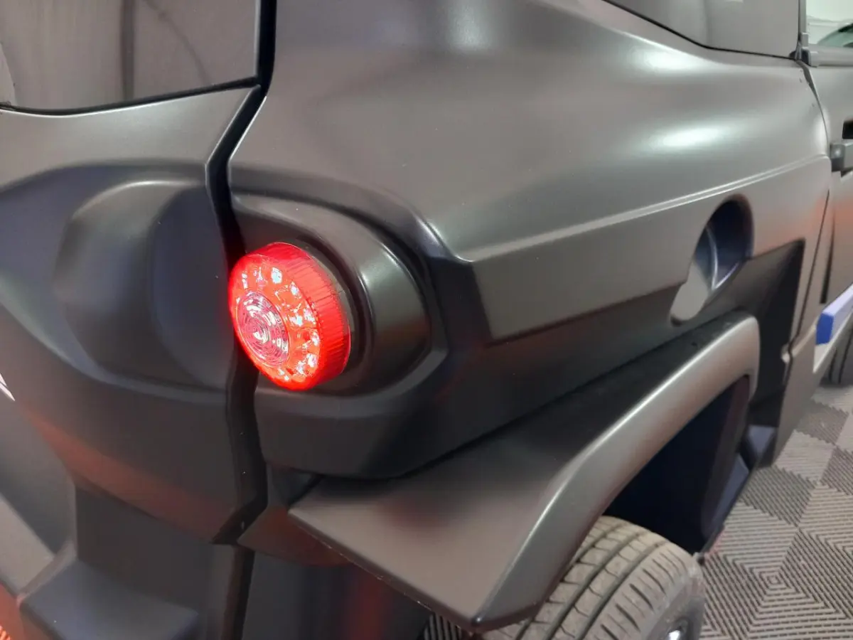 Gros plan sur le feu arrière droit rouge d’une Aixam Mega E-Scouty Evo bleu, soulignant ses lignes anguleuses.