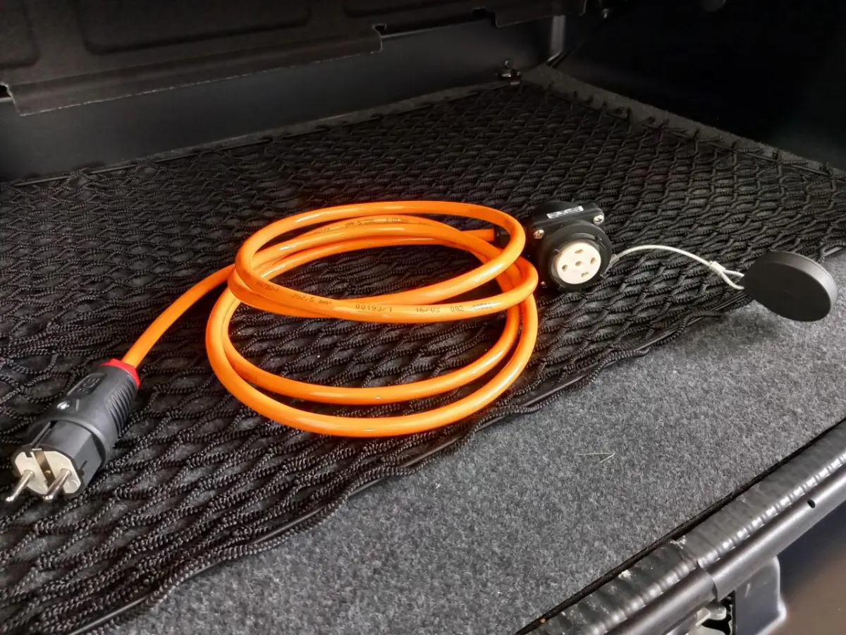 Câble de recharge orange enroulé dans le coffre d'une Aixam Mega E-Scouty Evo bleu électrique, vue intérieure arrière.