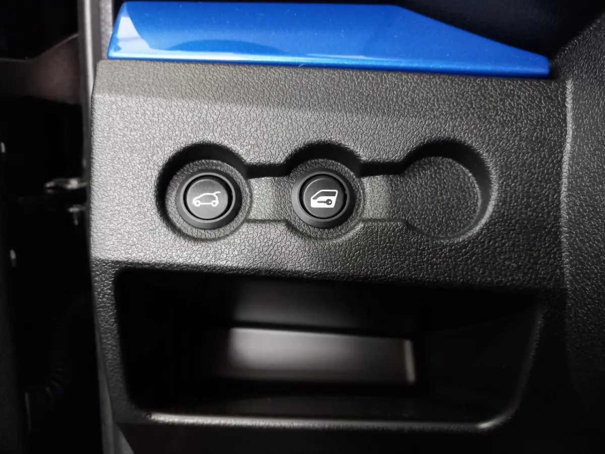 Gros plan sur les boutons d’ouverture du coffre et de la trappe à carburant dans l’habitacle d’une Aixam Mega bleu.