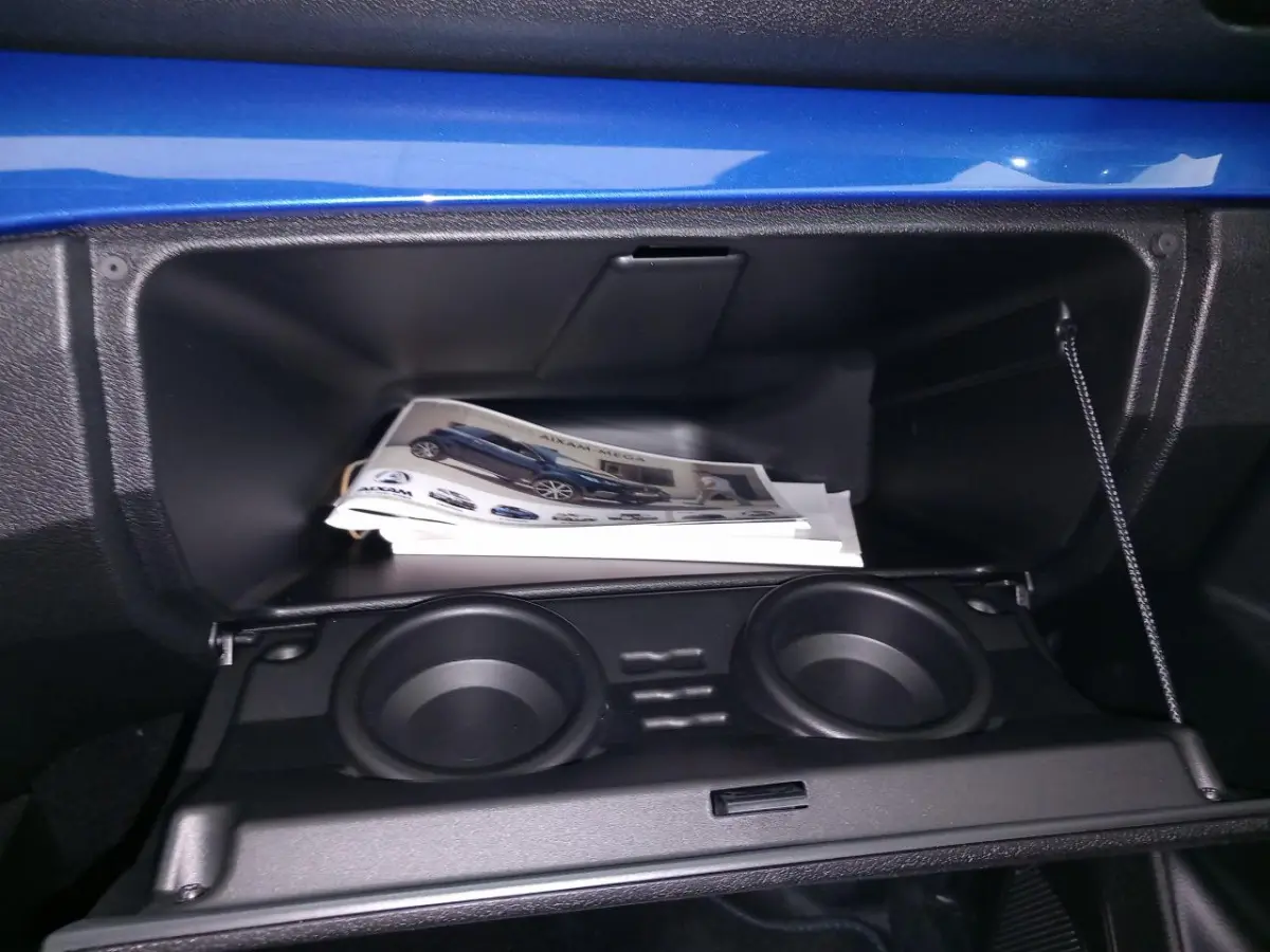 Intérieur de la boîte à gants ouverte d'une Aixam Mega bleu, avec porte-gobelets et documentation visible.