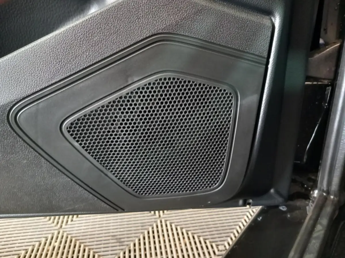 Gros plan sur la grille de haut-parleur intégrée à la porte intérieure noire d'un véhicule AIXAM MEGA bleu.