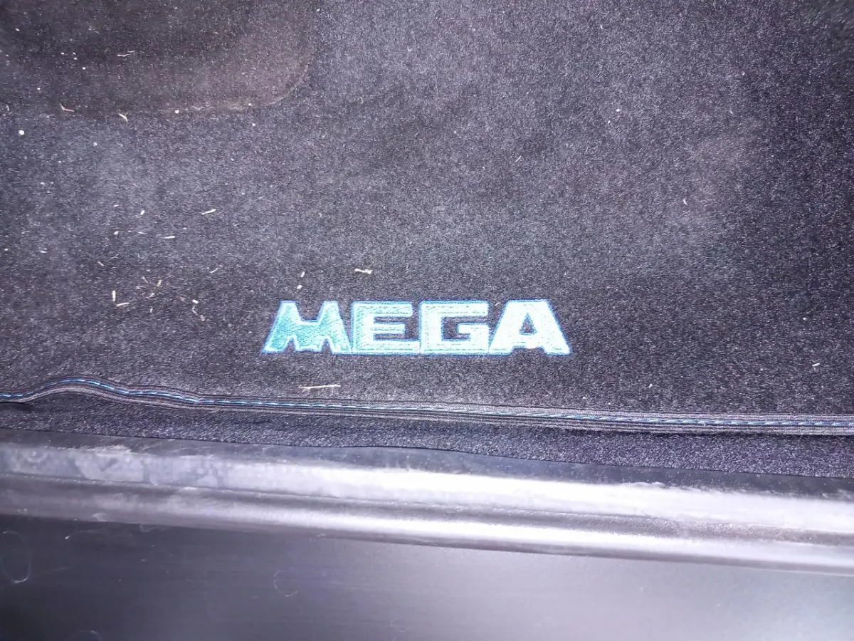 Gros plan sur le tapis de sol noir avec logo bleu "MEGA" à l'entrée côté conducteur d'un véhicule Aixam.