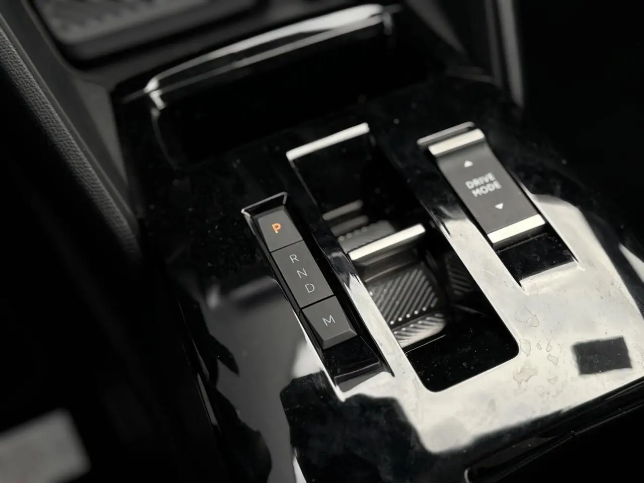 Gros plan sur la console centrale noire brillante de la Citroën C4 Hybrid 145, avec sélecteur de vitesses et bouton Drive Mode.