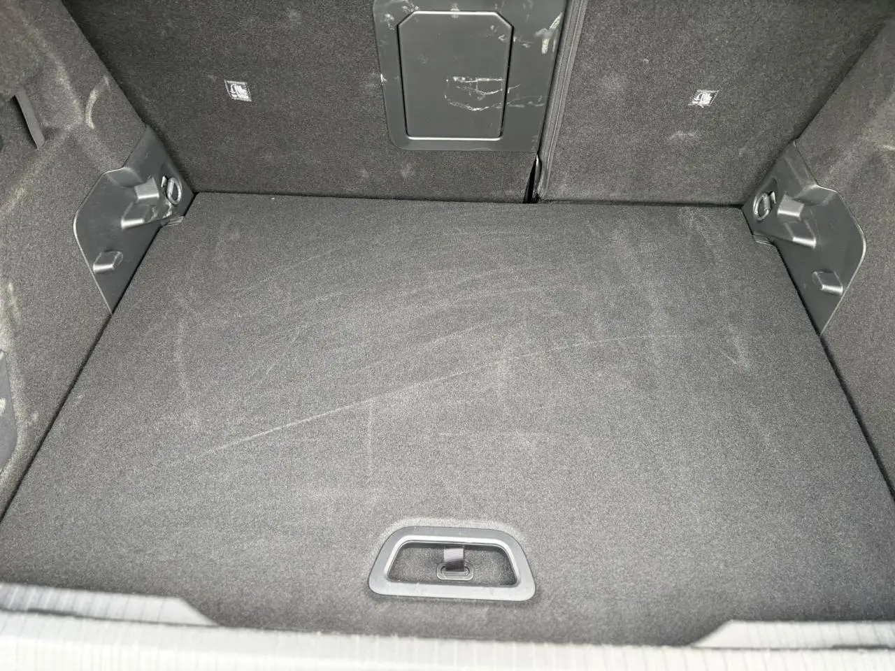 Coffre spacieux vu de face, revêtement tissu noir, avec trappe d'accès et fixations latérales visibles.