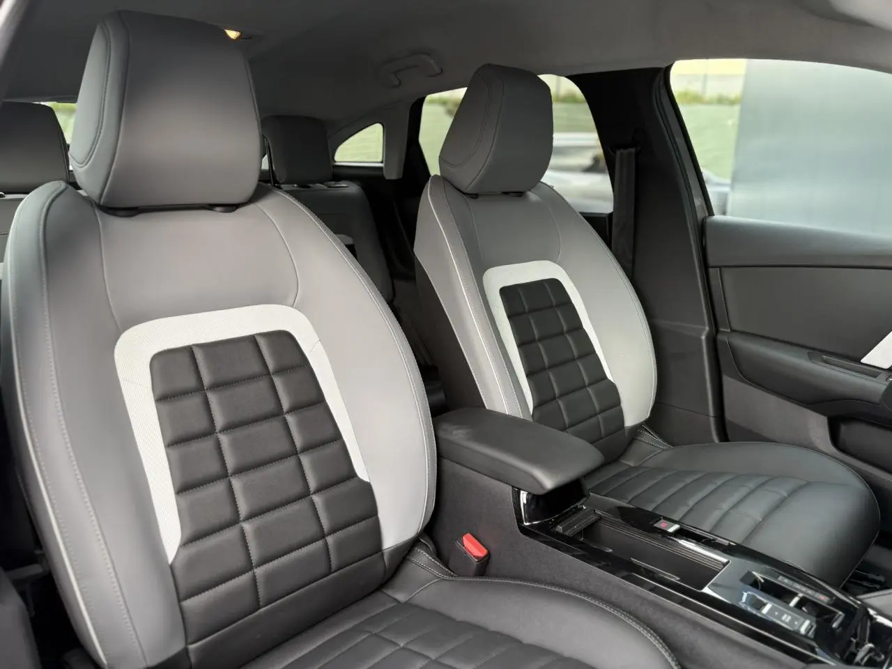 Vue intérieure des sièges avant gris clair et noir de la Citroën C4 Hybrid 2025 avec accoudoir central et console brillante.