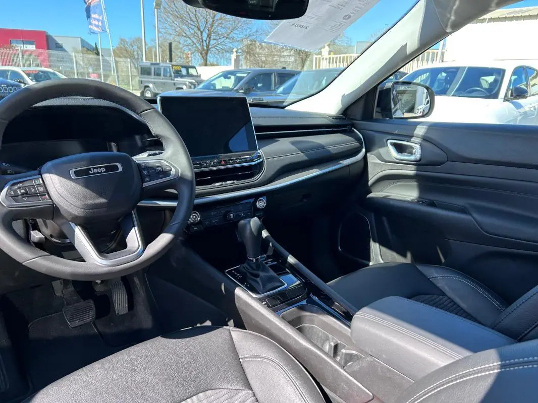 Vue intérieure côté conducteur du Jeep Compass gris 2024, avec volant multifonction, écran tactile et accoudoir central.