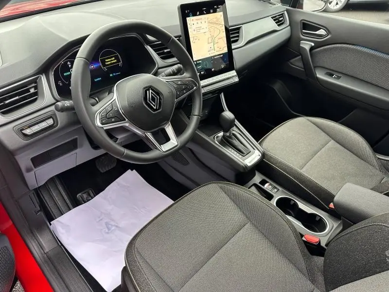 Vue intérieure avant droite du Renault Captur rouge 2025, volant multifonction et écran tactile vertical central.