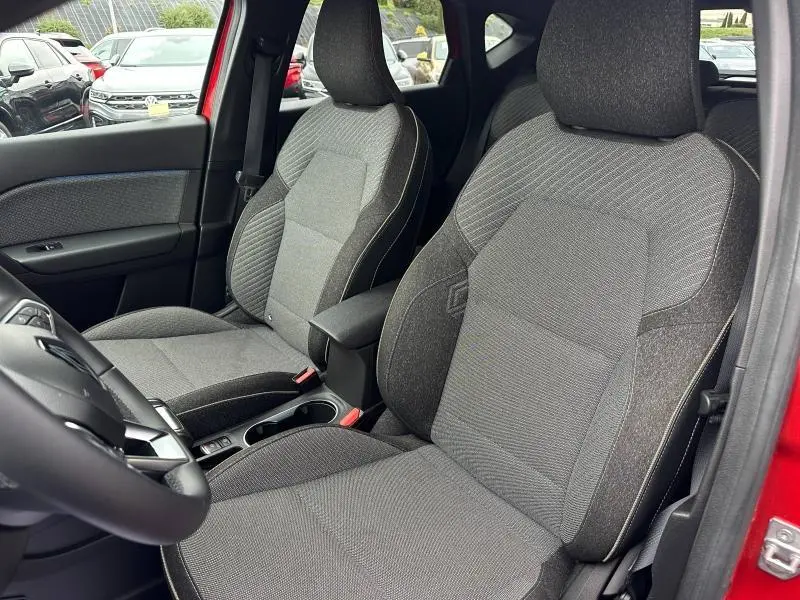 Vue intérieure avant du Renault Captur rouge 2025, sièges tissu gris avec accoudoir central et volant multifonction.