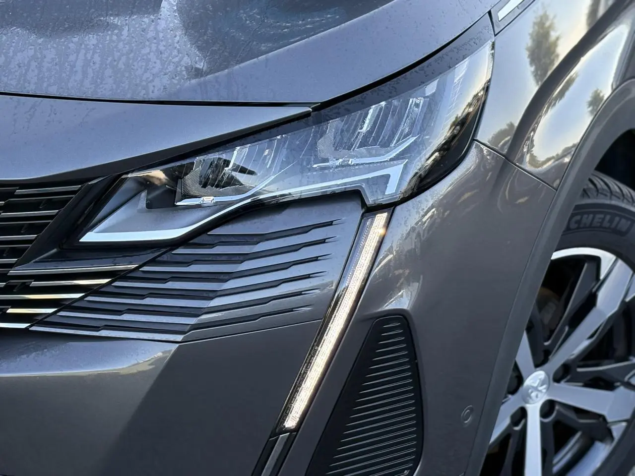 Gros plan sur le phare avant droit et la calandre d’un Peugeot 5008 gris Platinium avec jante alliage 18 pouces.