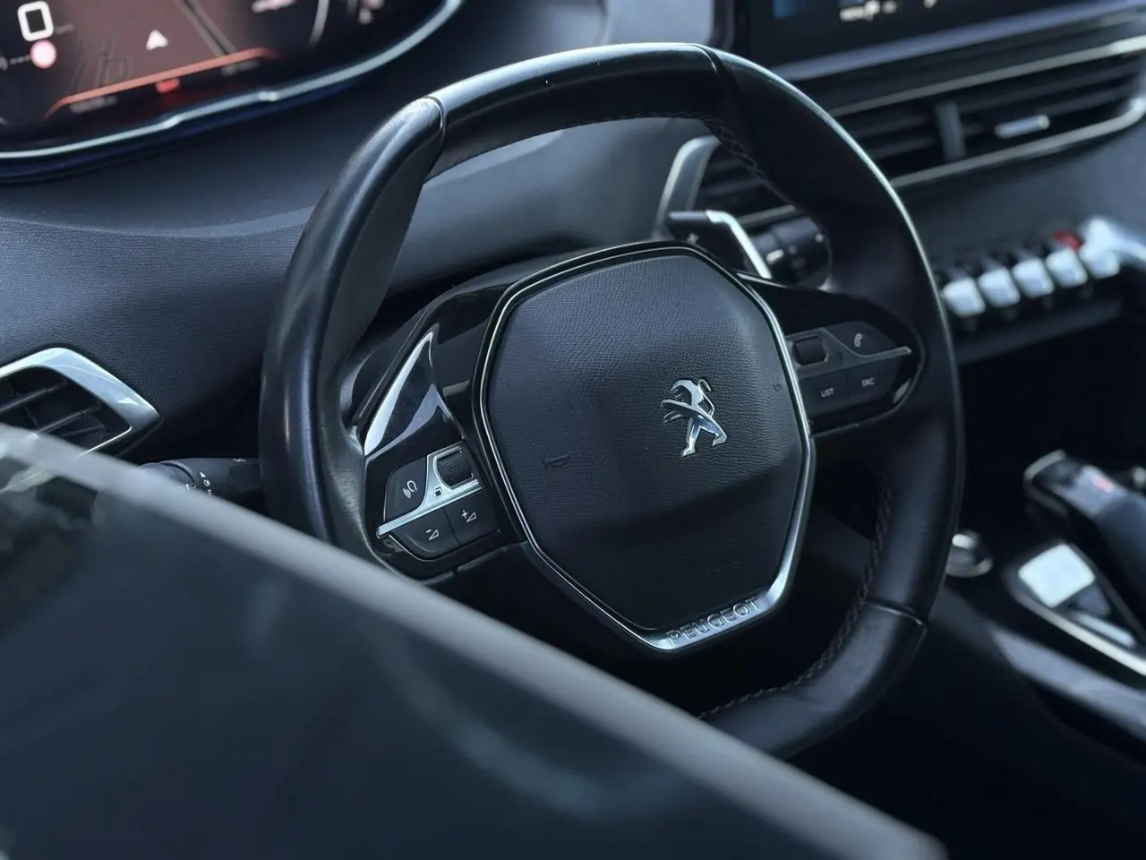 Gros plan sur le volant cuir noir du Peugeot 5008 2022, avec commandes intégrées et tableau de bord numérique visible.