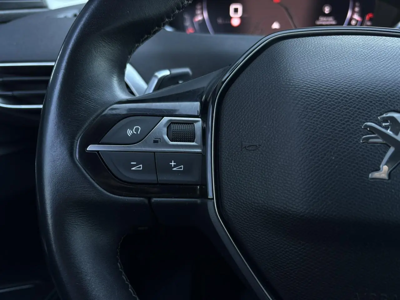 Gros plan sur le volant cuir noir du Peugeot 5008 2022 avec commandes audio et logo lion au centre.