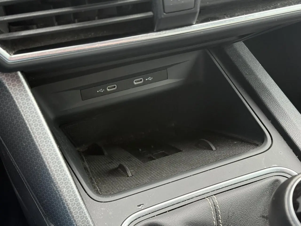 Gros plan sur la console centrale noire du SEAT LEON 1.5 TSI 115 Style, montrant les ports USB-C et le chargeur à induction.