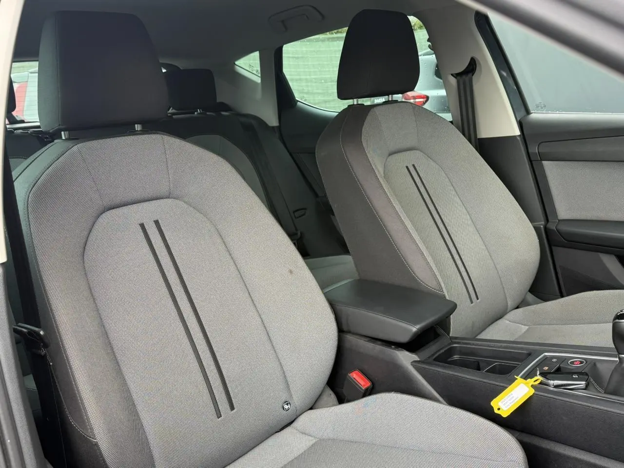 Vue intérieure côté avant droit du SEAT LEON 1.5 TSI 115 Style 2025 avec sièges tissu gris clair et accoudoir central noir.