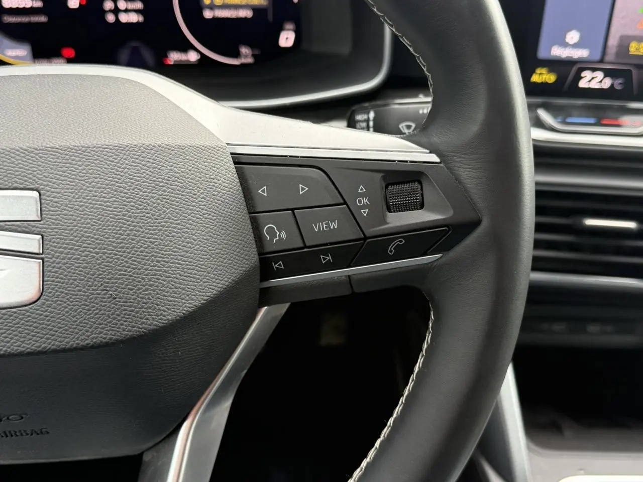 Gros plan sur le volant cuir multifonction noir de la SEAT LEON 2025 avec commandes intégrées et tableau de bord digital.