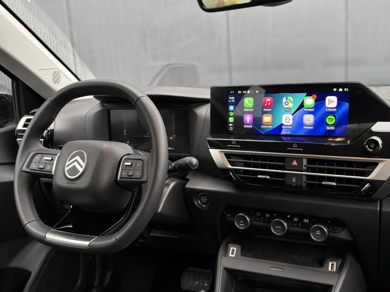 Vue intérieure centrée sur le volant Citroën et l’écran tactile 10" du tableau de bord du C4 Hybrid rouge Elixir.