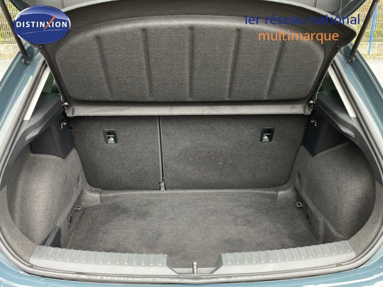 Coffre ouvert d’une SEAT LEON gris magnétique métal, vue arrière centrée montrant l’espace de chargement vide et doublé de tissu gris.