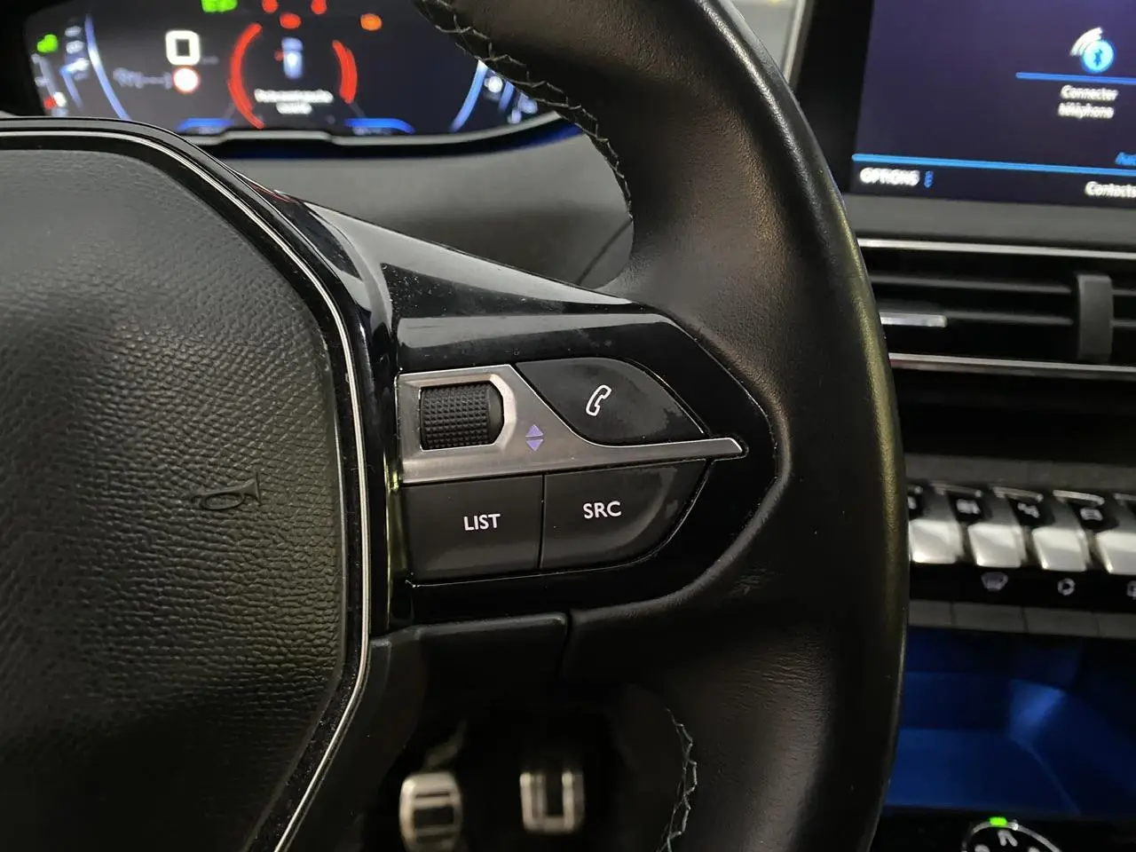 Gros plan sur les commandes au volant à droite en cuir noir du Peugeot 3008 gris Artense, avec tableau de bord et écran tactile en arrière-plan.