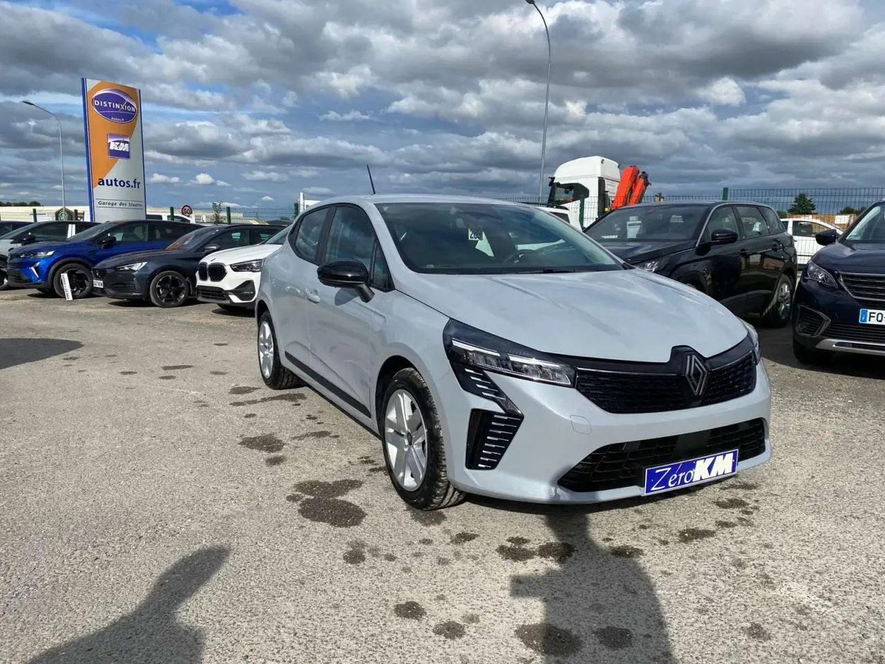 Renault Clio gris Rafale vue 3/4 avant droit, avec calandre noire et feux LED distinctifs, stationnée en extérieur.