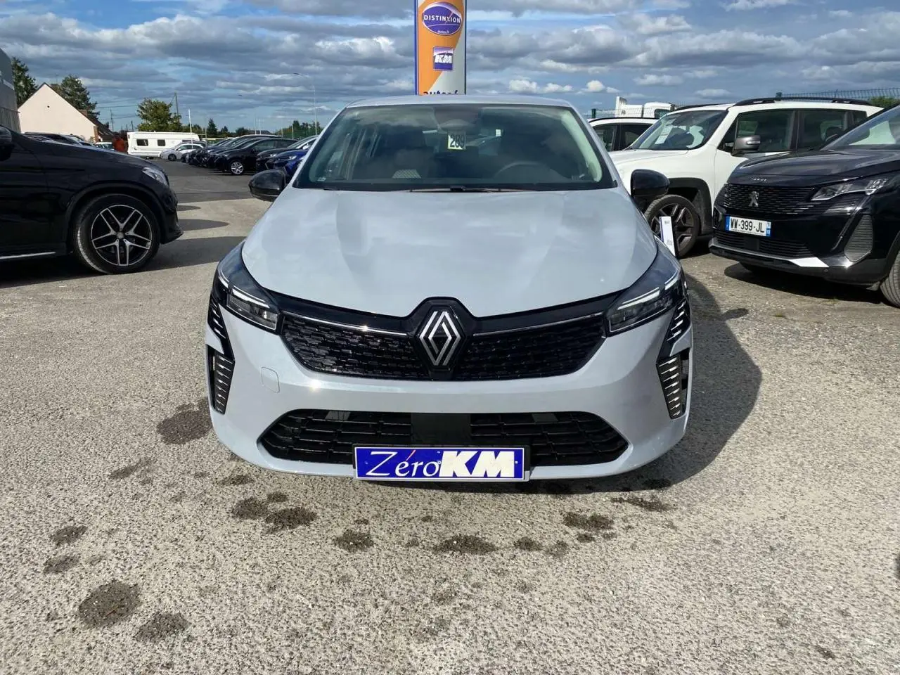 Vue frontale d'une Renault Clio 2025 gris Rafale avec calandre noire et phares LED allumés sur parking.