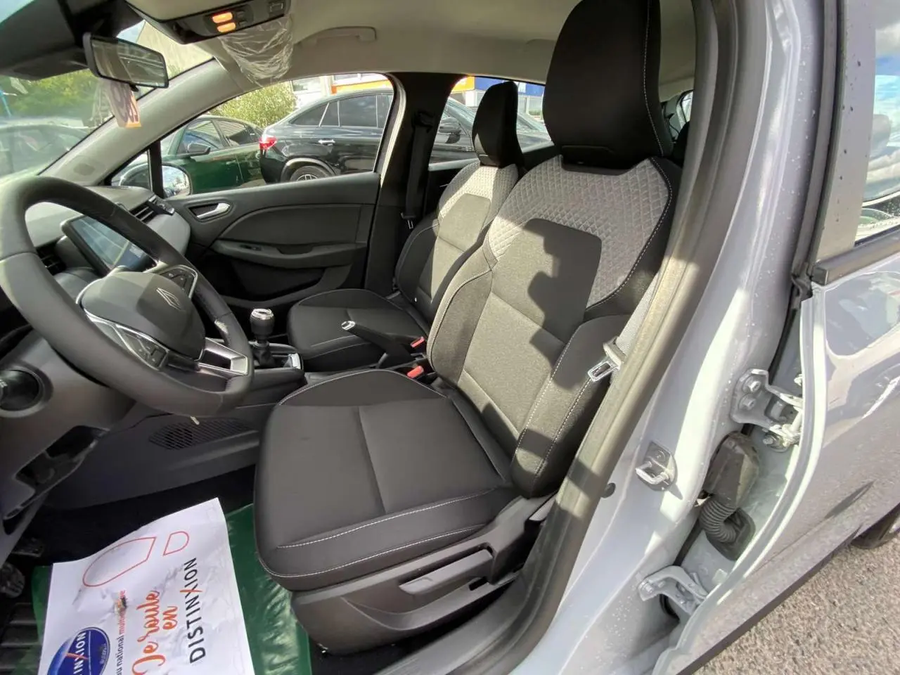 Intérieur de la Renault Clio 2025 gris Rafale, vue côté conducteur, sièges noirs avec surpiqûres blanches et volant multifonction.