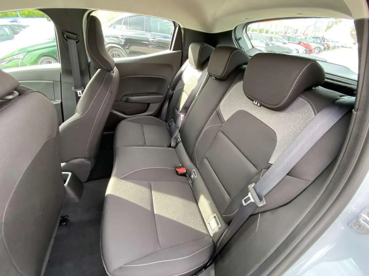 Vue intérieure arrière droite de la Renault Clio 2025 gris Rafale, montrant les sièges arrière en tissu noir avec surpiqûres blanches.