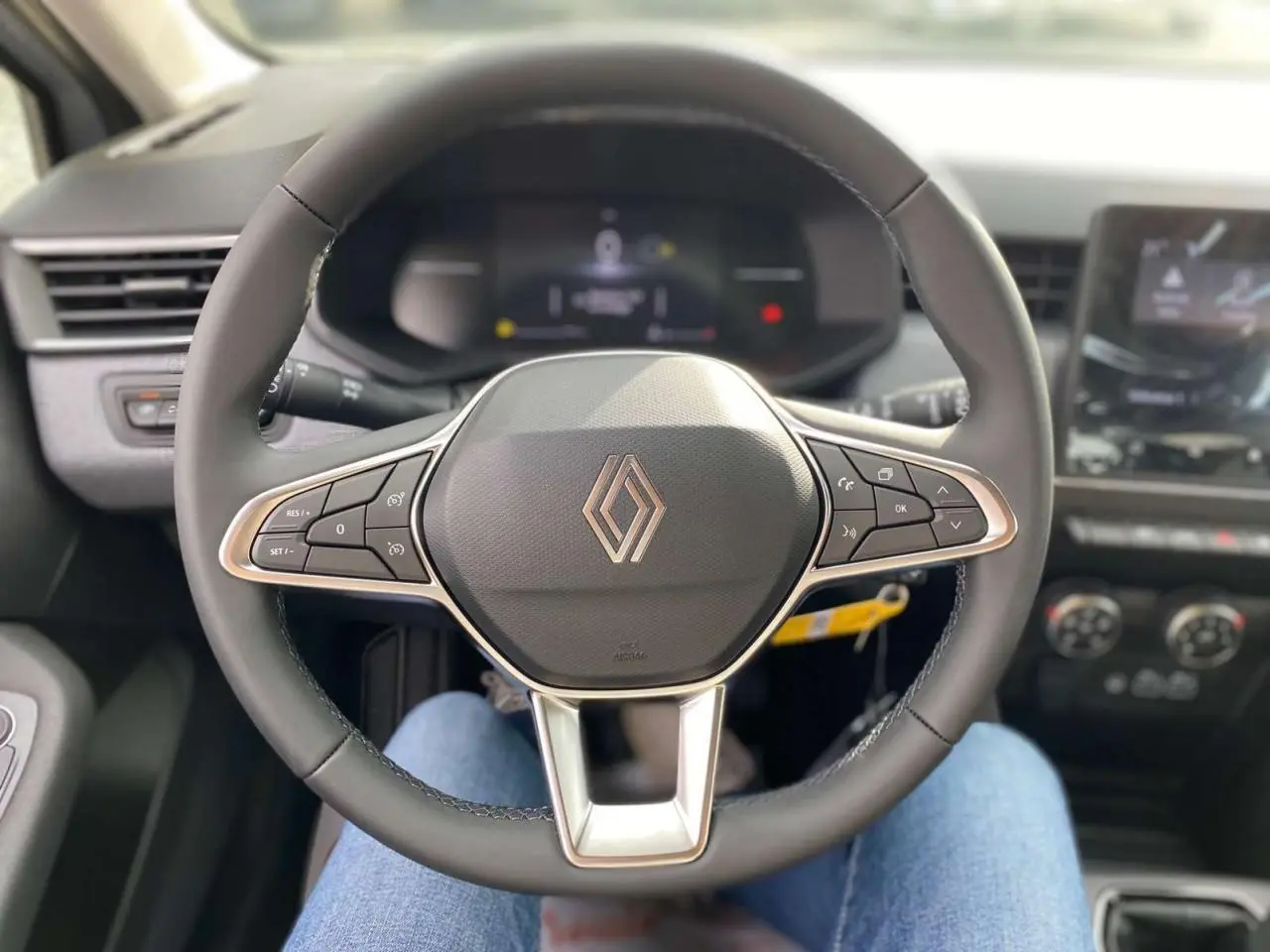 Vue rapprochée du volant multifonction noir de la Renault Clio 2025 avec tableau de bord et écran tactile en arrière-plan.