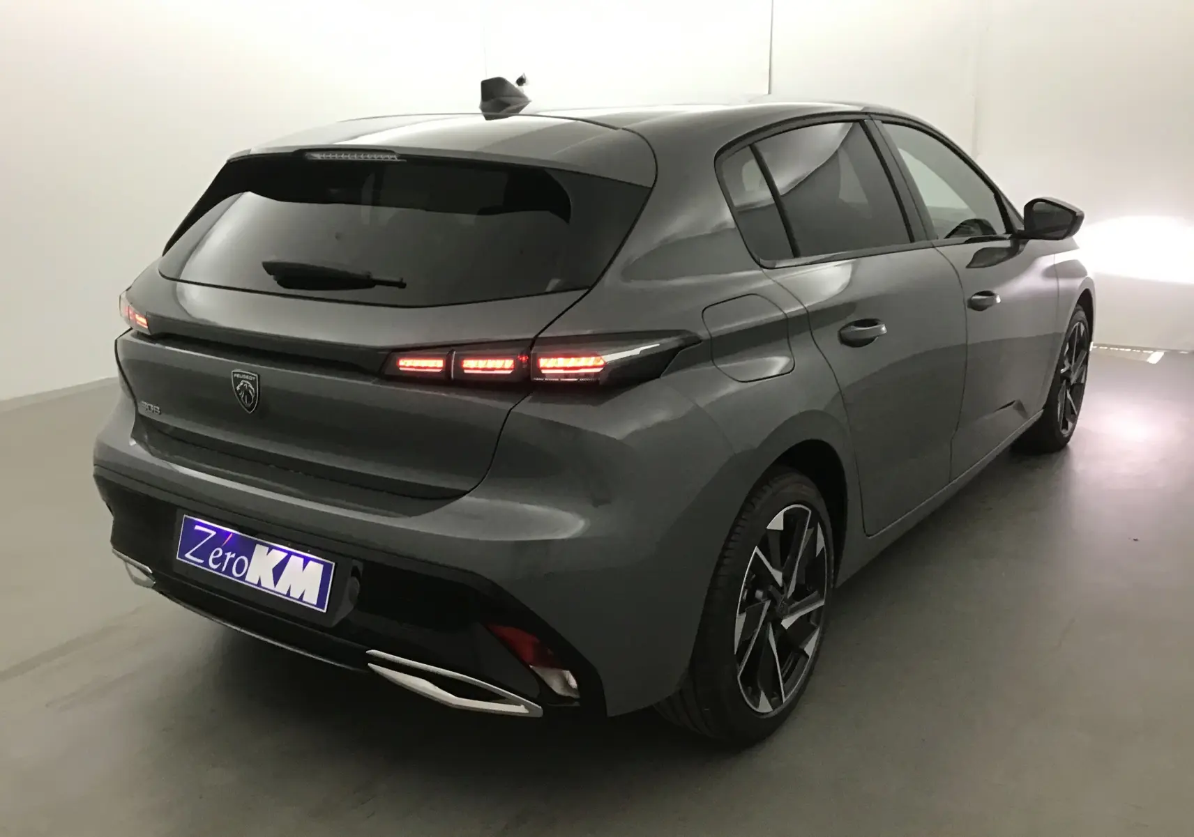 Peugeot 308 gris Sellenium en 3/4 arrière droit, feux arrière allumés et jantes alliage noires distinctives.