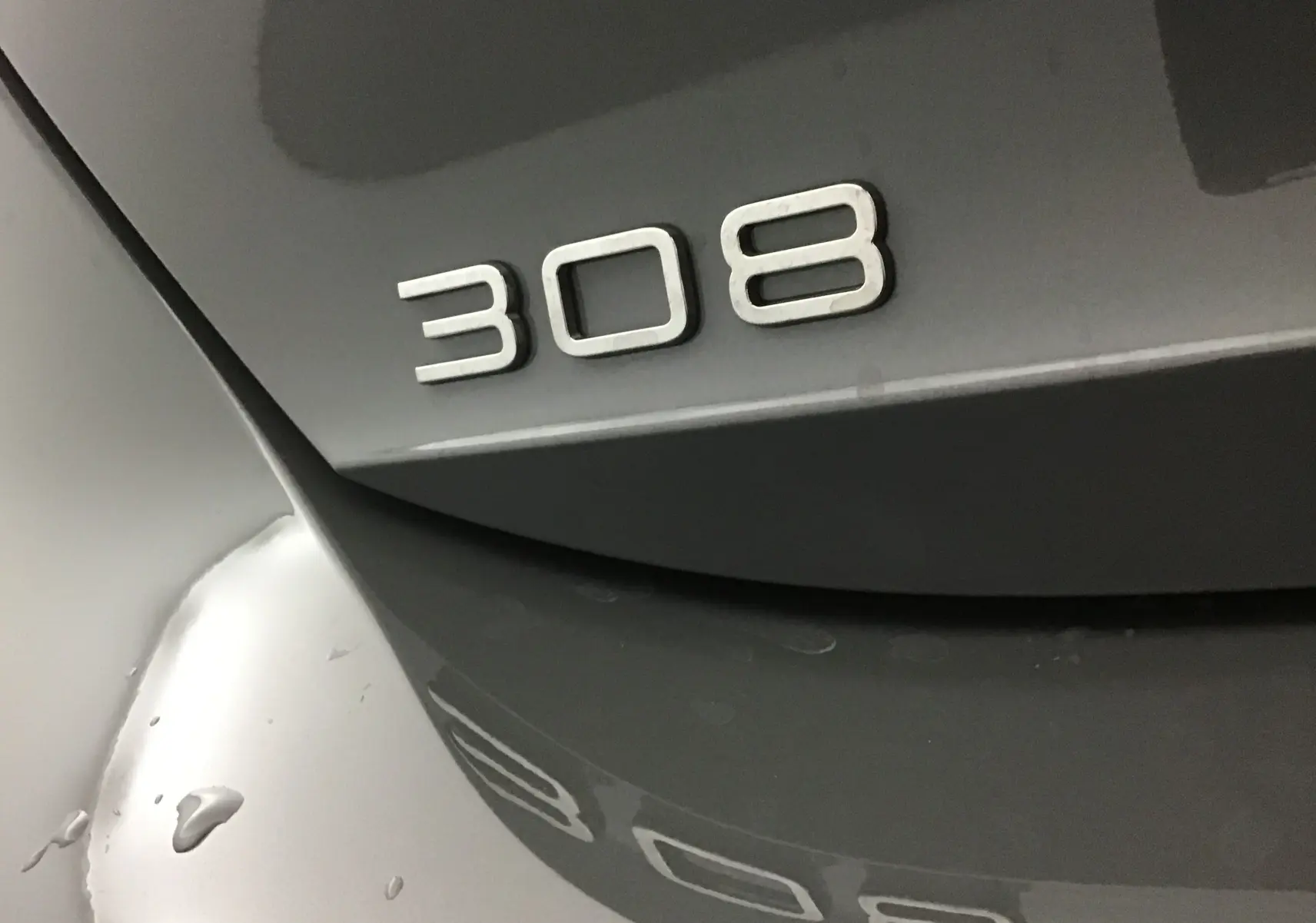 Gros plan sur l'arrière gris Sellenium d'une Peugeot 308 avec le logo 308 en relief visible.
