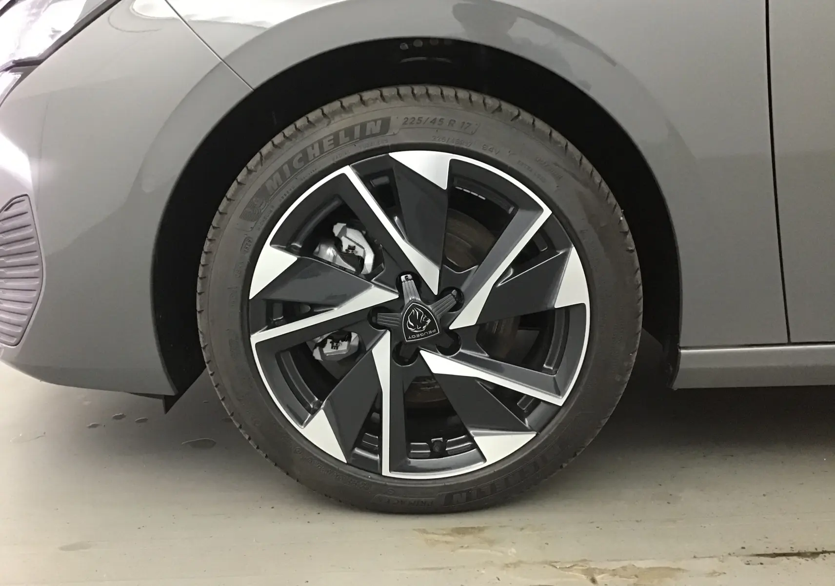 Gros plan sur la roue avant gauche d'une Peugeot 308 gris Sellenium avec jante alliage noire et argentée.