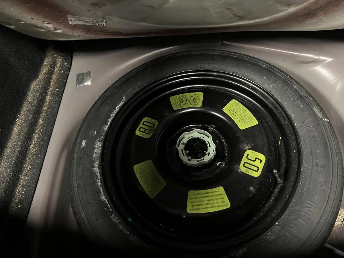 Gros plan sur la roue de secours galette noire dans le coffre violet d'une DS3 1.6 BlueHDi So Chic 2016.