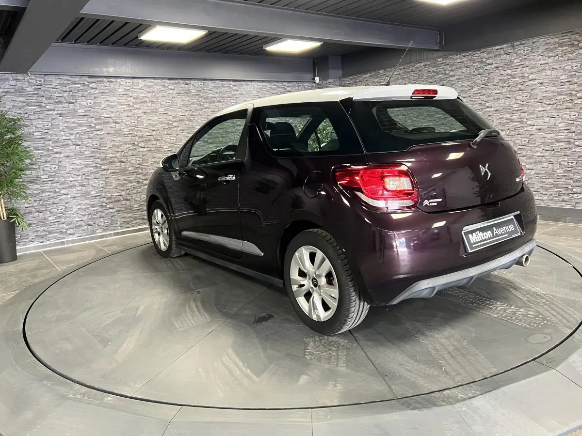 Vue 3/4 arrière droite d'une DS3 violet foncé avec toit blanc et canule d'échappement chromée en showroom.
