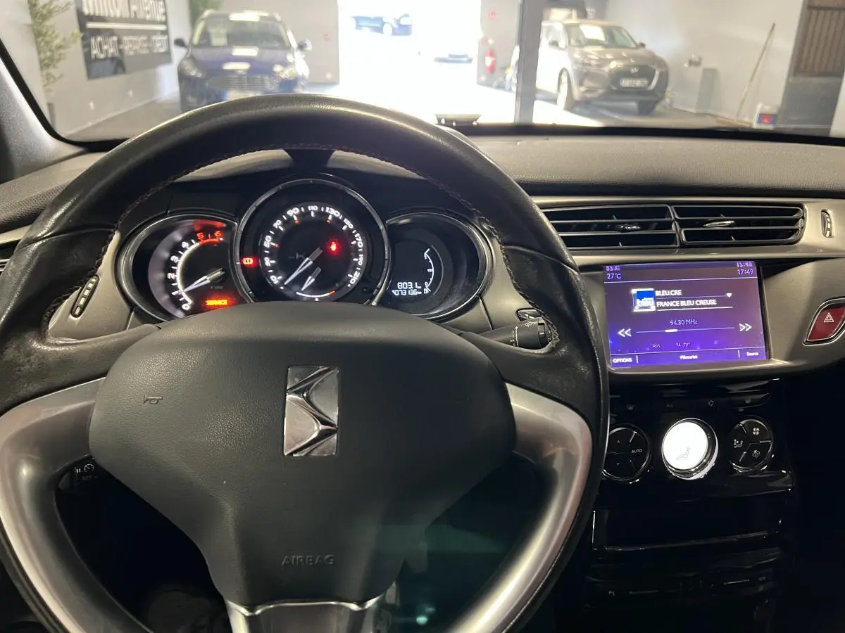 Vue intérieure du tableau de bord et volant cuir noir de la DS3 1.6 BlueHDi So Chic 2016 avec écran tactile allumé.