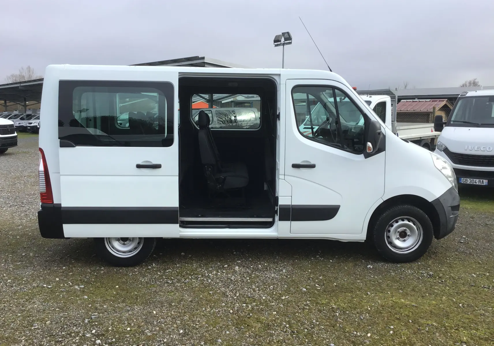 Vue de profil côté gauche d’un Renault Master Combi III blanc 2017 avec porte coulissante ouverte révélant les sièges passagers.