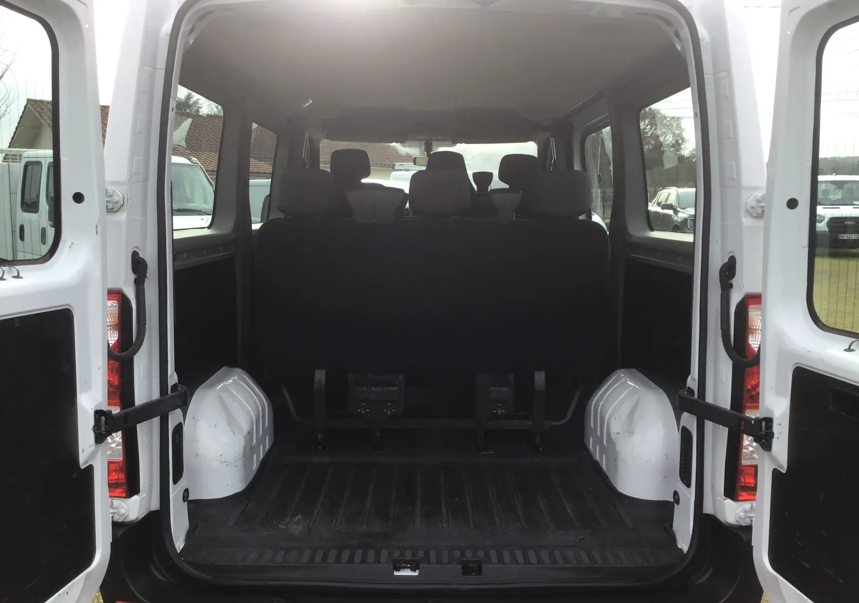 Vue arrière intérieure du Renault Master Combi III blanc 2017, portes ouvertes, montrant l'espace de chargement et les sièges passagers.