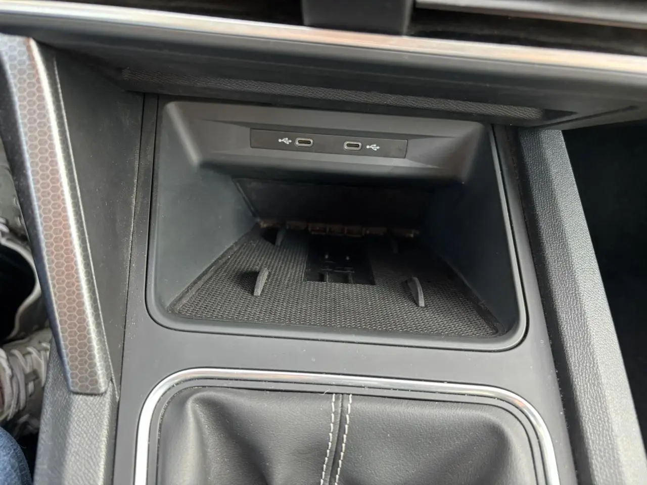 Vue rapprochée de la console centrale du SEAT LEON 2.0 TDI 115 Style 2025, avec ports USB et surface de rangement noire.