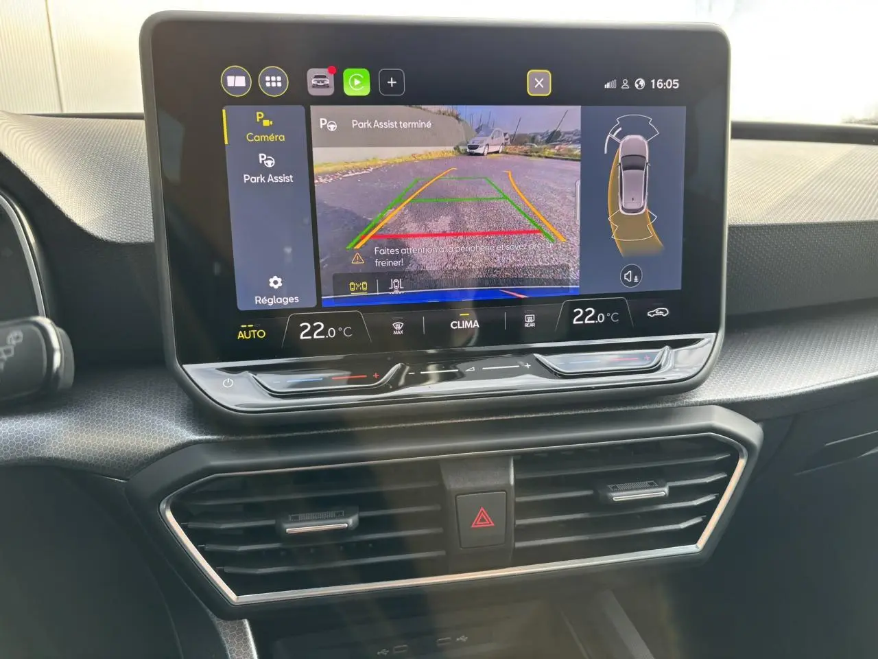 Vue rapprochée de l’écran central du SEAT Leon 2025 bleu Fjord affichant l’aide au stationnement avec caméra et réglages climatiques.