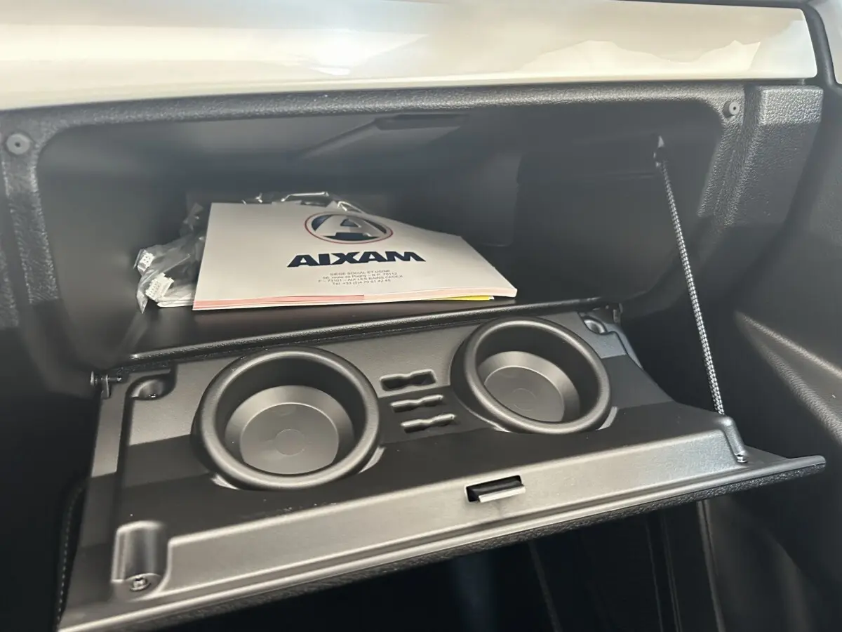 Intérieur de l’AIXAM AMBITION 0.5 CROSSOVER PREMIUM 2026, boîte à gants ouverte avec porte-gobelets intégrés.