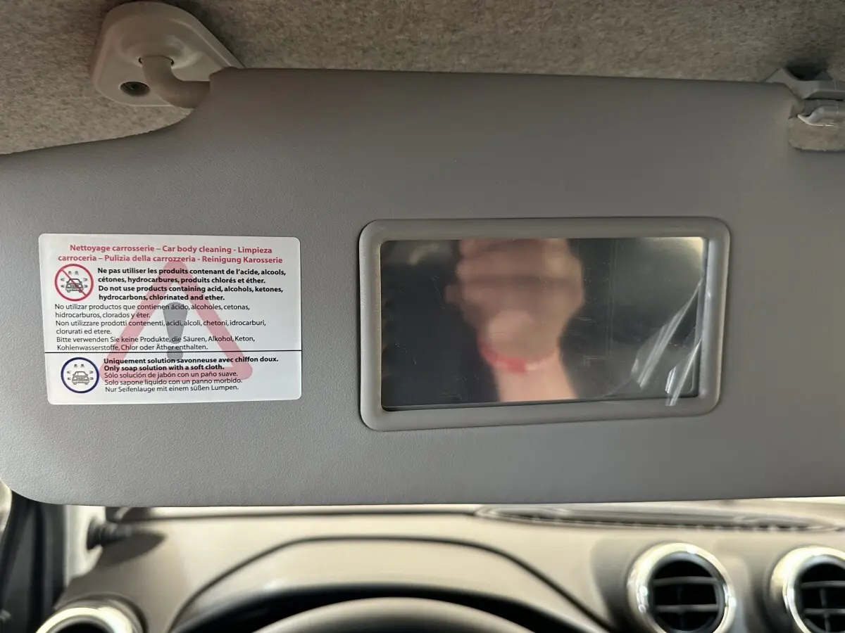 Vue intérieure centrée sur le pare-soleil avec miroir et consignes de nettoyage, tableau de bord beige visible en bas.