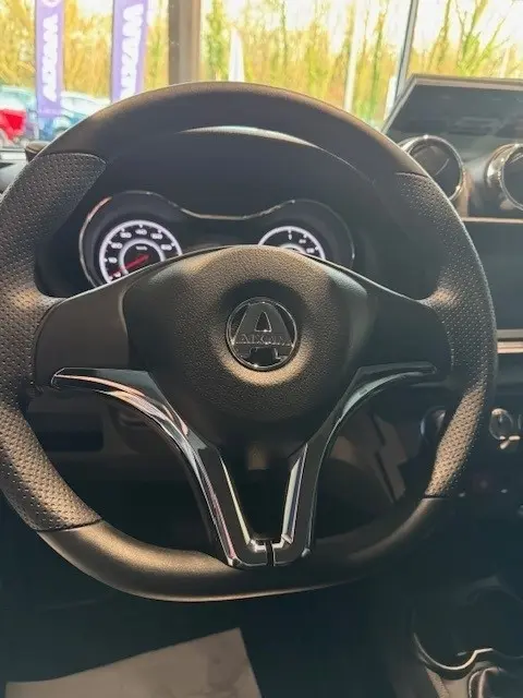 Vue rapprochée du volant noir de l'AIXAM AMBITION 0.5 CROSSOVER PREMIUM 2026 avec tableau de bord éclairé en arrière-plan.