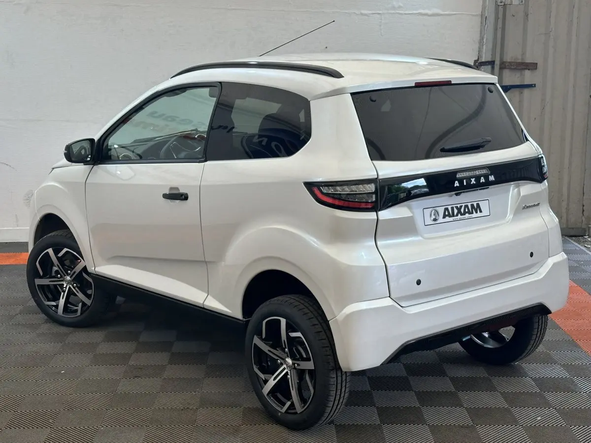Vue 3/4 arrière droite d'une Aixam Ambition 0.5 Crossover Premium blanche avec jantes noires et rétroviseur caméra côté gauche.