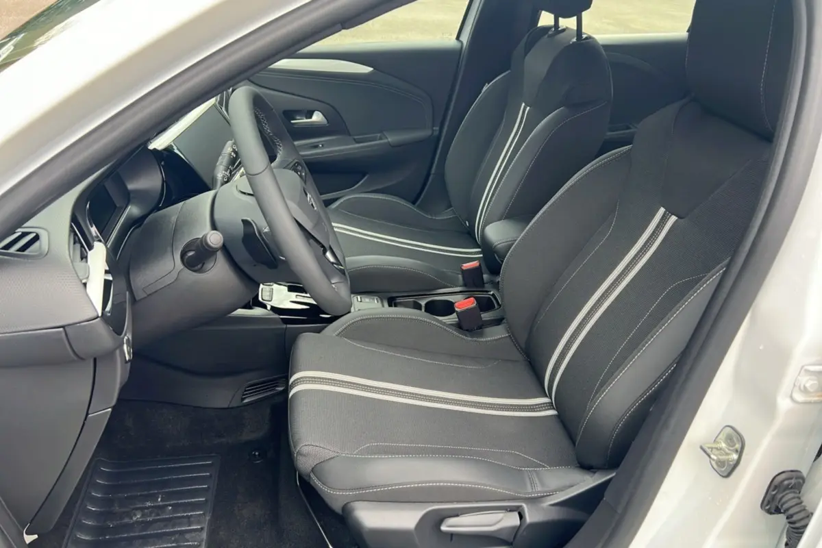 Vue intérieure côté conducteur de l’Opel Corsa blanc kontur, montrant les sièges noirs avec surpiqûres claires et le volant multifonctions.