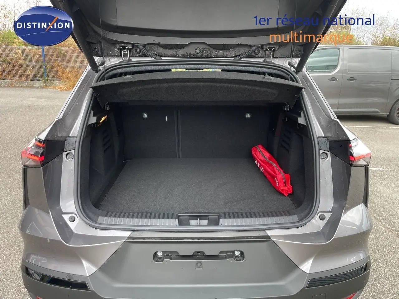 Coffre ouvert vu de l'arrière d'une Renault Symbioz gris cassiopée métal, avec un kit de secours rouge à droite.