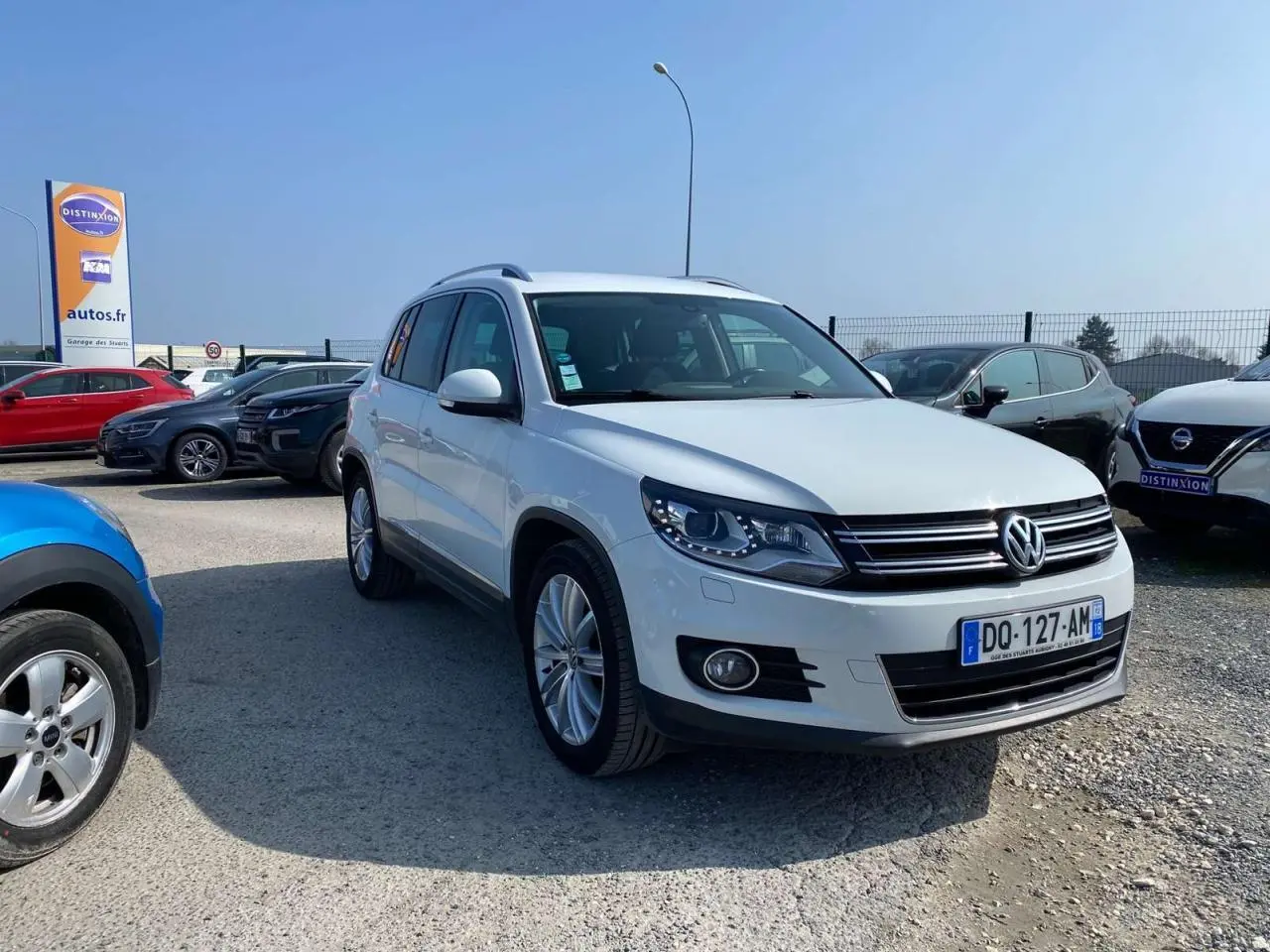 Volkswagen Tiguan blanc vu en 3/4 avant droit sur parking avec jantes alliage et calandre noire chromée.