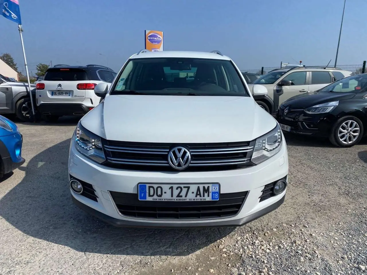 Volkswagen Tiguan blanc vu de face, avec calandre noire et feux avant allumés au soleil.